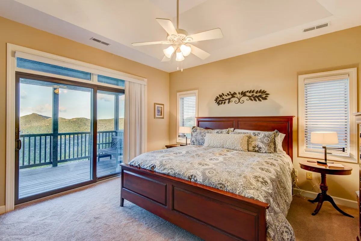 A tranquil king suite featuring a king-sized bed, sliding glass door leading to a balcony, decorative wall art, and a cozy nightstand with lamp. The room is bathed in natural light, creating a serene and inviting atmosphere ideal for restful privacy.