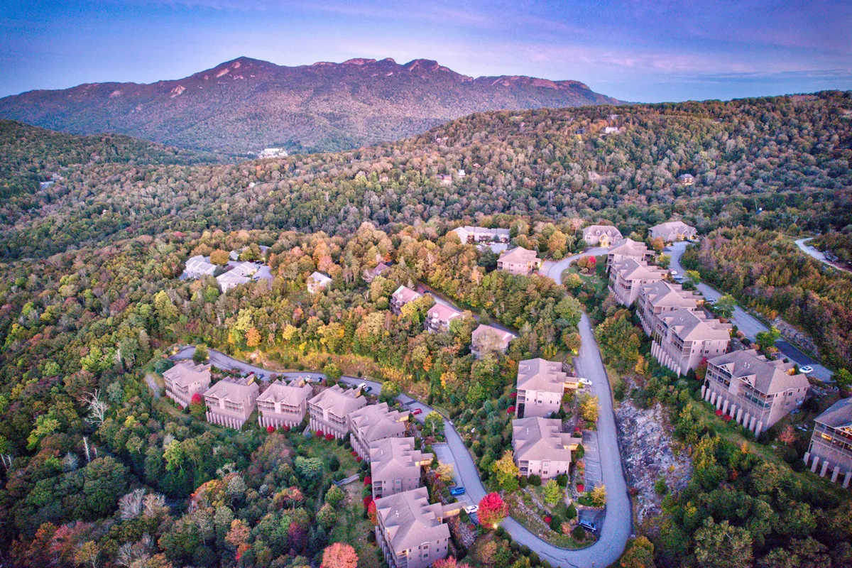 This exterior image captures a tranquil mountain setting with rows of houses nestled along a winding road, framed by vibrant autumn foliage and majestic mountains in the background. The scene hints at nearby walking trails and the outdoor adventures that await just beyond the condo.