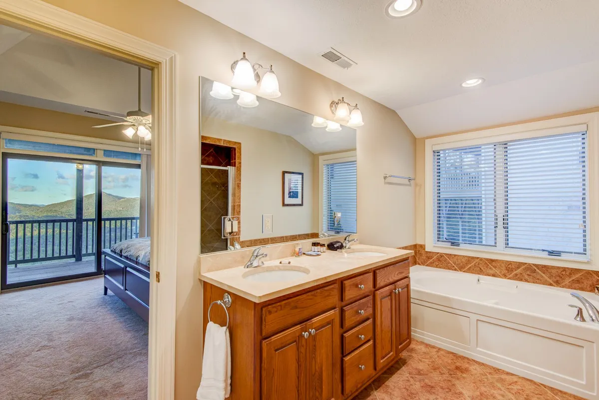 A stylish bathroom with a double vanity sink, large window, and a bathtub, offering a glimpse of the tranquil surroundings outside. The space is bright, modern, and perfect for relaxing baths or morning routines.