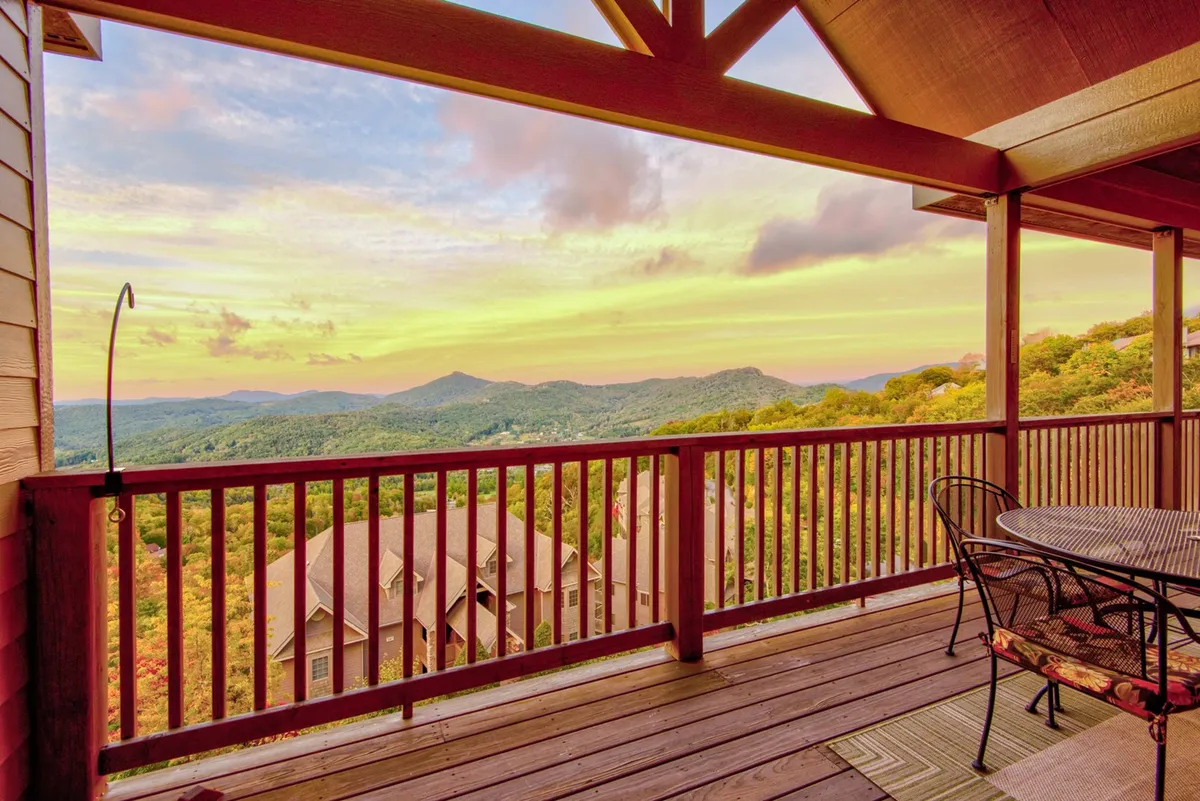 A tranquil deck with outdoor seating, offering unobstructed views of the mountain range and a colorful sunset sky. The deck’s railing frames the landscape, making it an ideal spot for coffee at dawn or evening toasts.