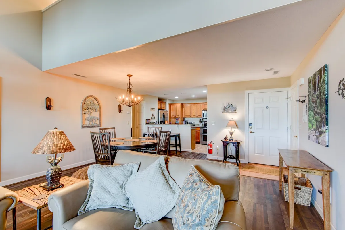 A seamless flow between a comfortable sofa, dining area, and modern kitchen, all bathed in natural light. Decorative wall art and thoughtful furnishings create an inviting, homey atmosphere suited for gatherings and shared meals.