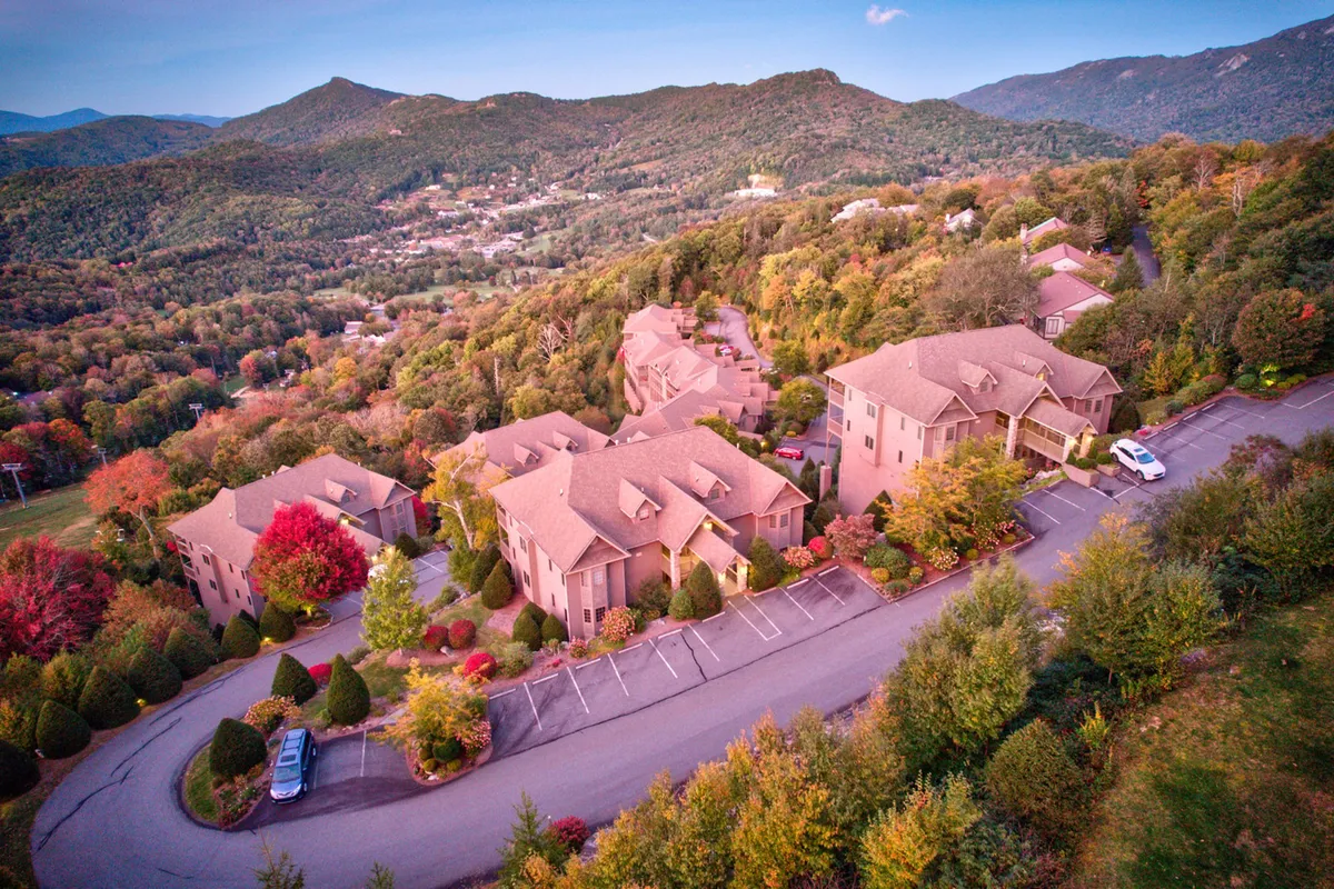 A serene view of a residential area with mountains rising in the background and vibrant fall trees in the foreground. The road leading into the mountains suggests easy access to hiking and ski adventures, reinforcing the property's gateway-to-adventure appeal.