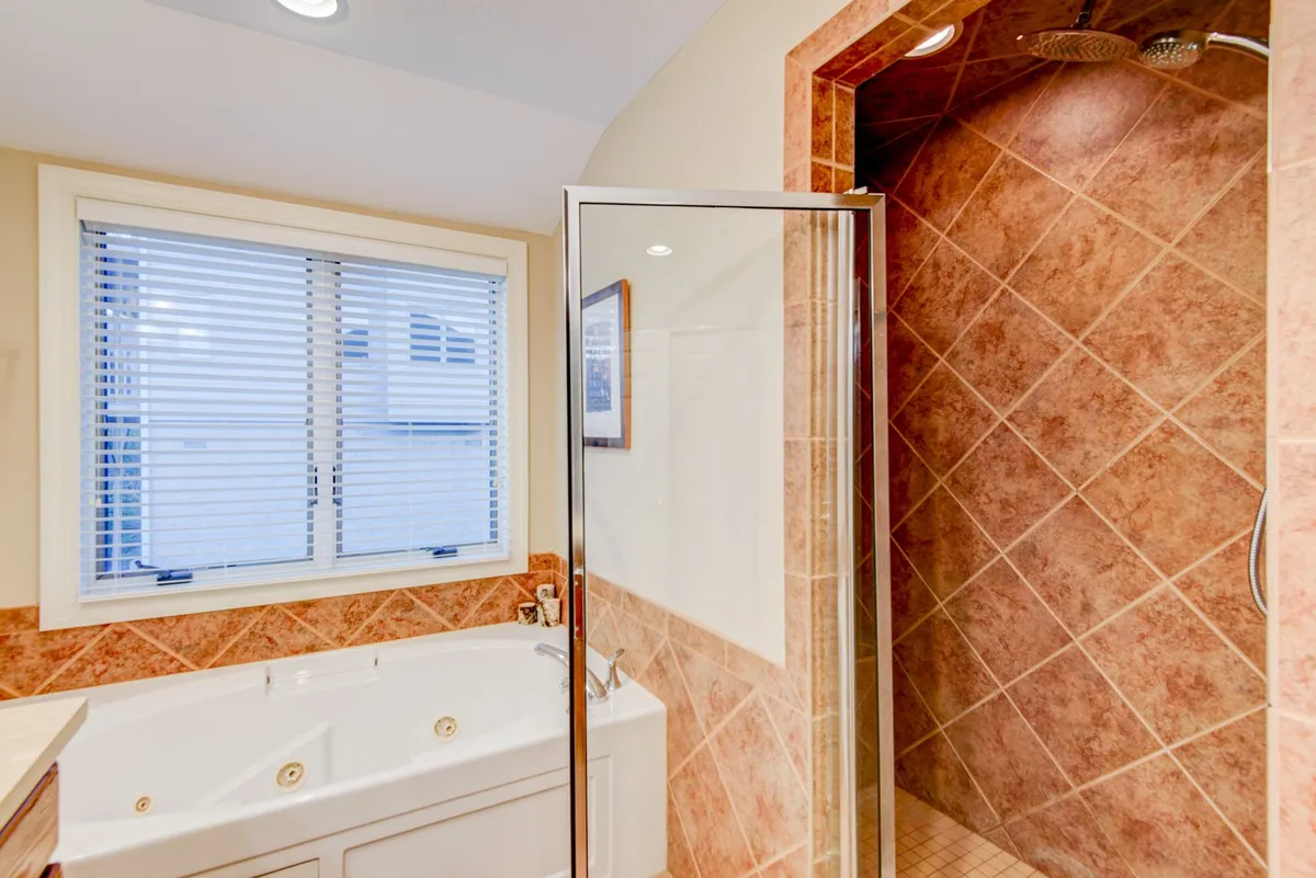 This image features a luxurious whirlpool tub and a glass shower enclosure, illuminated by natural light through a window with blinds. The bathroom is designed for relaxation and post-adventure recovery.