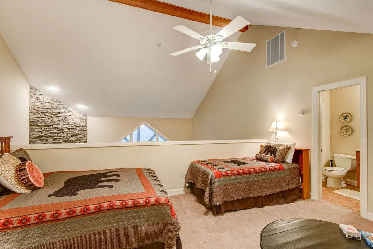A cozy bedroom with two beds dressed in patterned blankets, a striking stone feature wall, and a large window letting in ample daylight. The setting is warm and comfortable, perfect for friends, family, or kids.