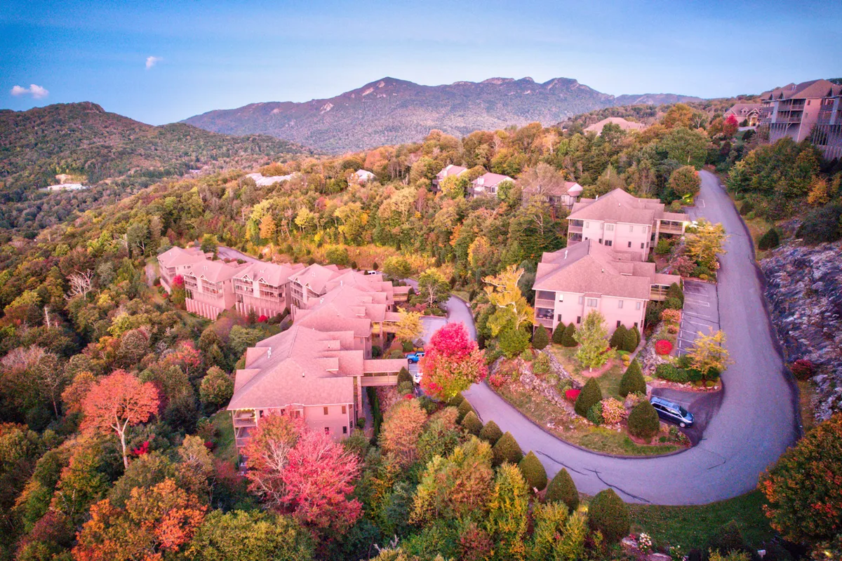 A vibrant exterior scene with colorful autumn trees, scenic mountain views, modern buildings, and well-maintained community pathways. The setting invites hiking, nature walks, and outdoor exploration right from the doorstep.
