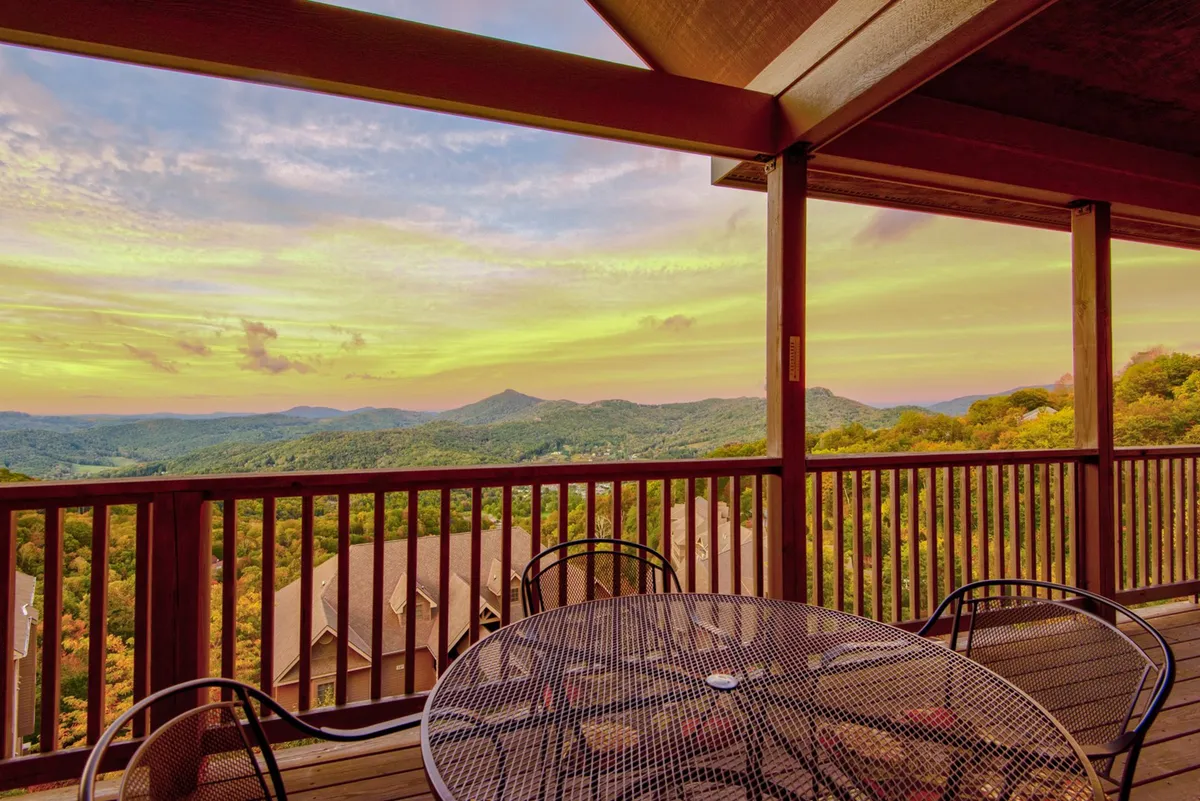 A table with chairs set outdoors overlooks a stunning mountain landscape and sunset sky. The scene captures a sense of tranquility and togetherness, ideal for al fresco dining, sharing stories, or socializing with loved ones as the day ends.