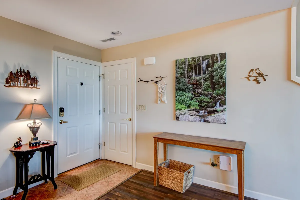 This image showcases a welcoming entryway with a wooden table, nature-themed wall art, and a table lamp. The scene conveys a sense of arrival and transition from outside to inside, with decorative items that add personality and warmth.