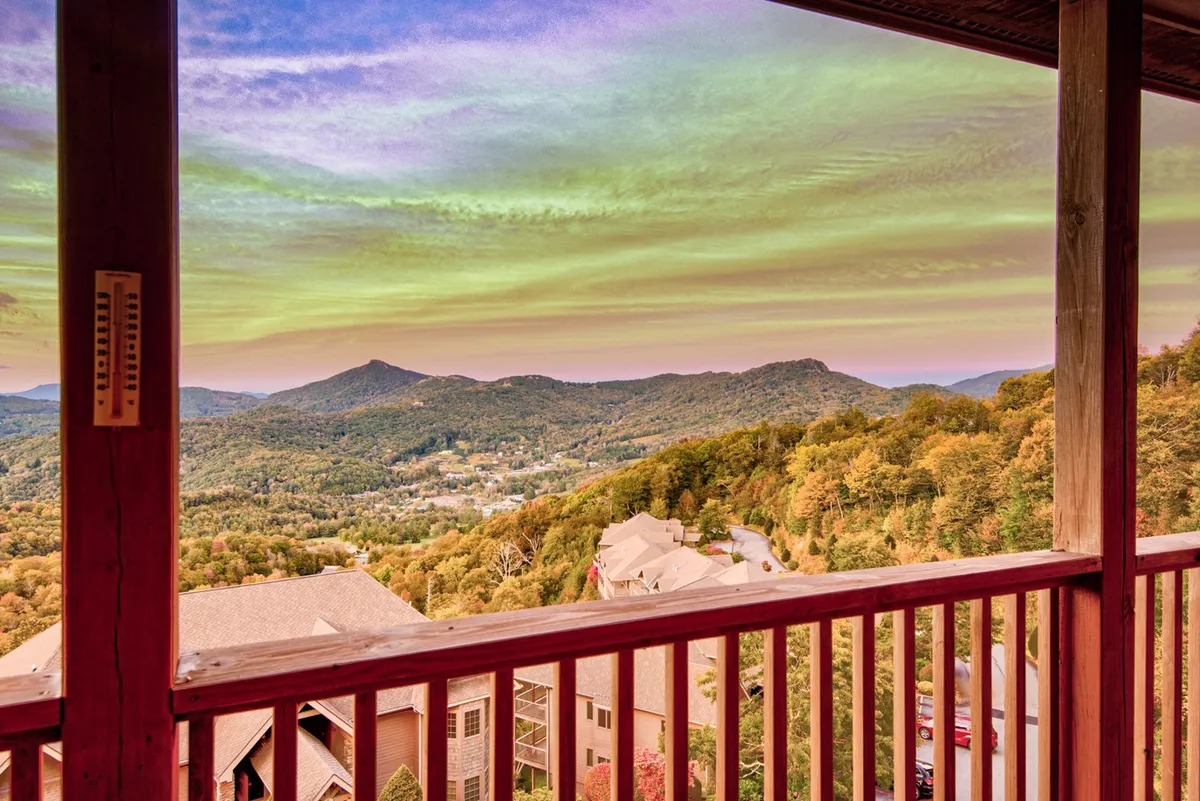 A tranquil view from a balcony or deck overlooking a sweeping mountain range and valley, with a wooden railing in the foreground. The colorful sky evokes a peaceful sunset, and the setting feels ideal for relaxing, gathering with loved ones, or simply admiring the landscape. The image emphasizes the region's stunning vistas and relaxing atmosphere.