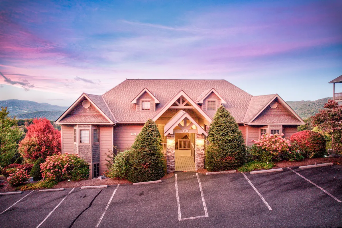 An inviting exterior scene showing the main entrance to the property, bordered by landscaped gardens and framed by a stunning mountain view. The area is ideal for family gatherings, outdoor barbecues, or simply soaking in the serene surroundings. The image conveys the property's connection to the outdoors and its mountain setting.