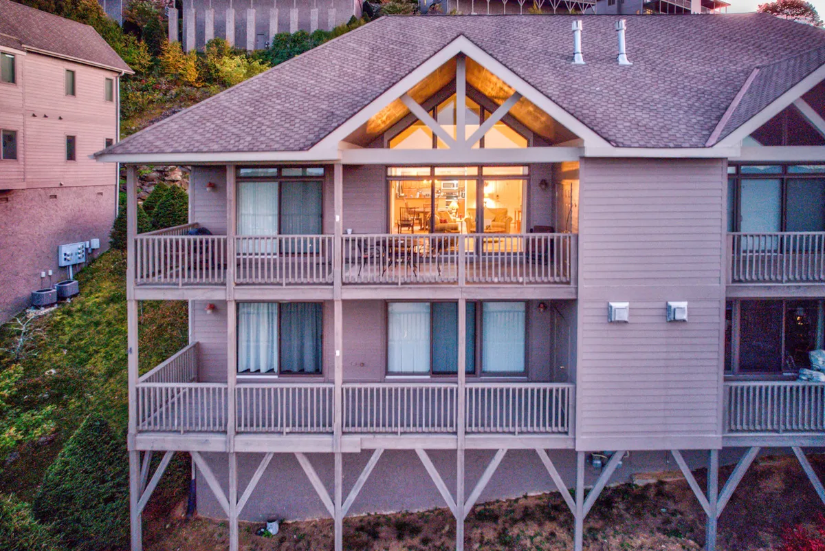 The condo's exterior is showcased with its inviting balconies and large windows, set against a backdrop of mountain views and warm sunset hues. The architectural details and outdoor space evoke opportunities for family gatherings, relaxing after a day outdoors, and enjoying the scenic environment.