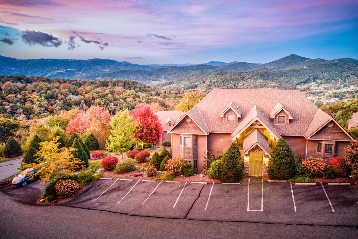 The image showcases the exterior of a stylish condo perched on Sugar Mountain, framed by vibrant, colorful trees and a sweeping mountain backdrop. The scene feels tranquil and inviting, ideal for outdoor gatherings, sunset viewing, and soaking in nature's beauty.