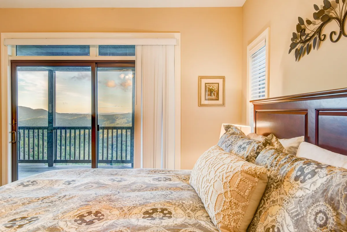 A cozy bedroom with a comfortable bed facing large sliding glass doors that open to a private balcony. Through the windows, guests enjoy sweeping mountain views—the perfect spot to wake up to a sunrise or enjoy a peaceful evening after a day of exploration.